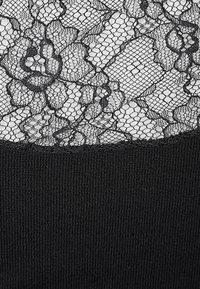 Schwarzes Spitzenoberteil mit floralen Mustern am oberen Teil, verbunden mit einem einfarbigen schwarzen Stoff am unteren Teil, mit einer strukturierten, gerippten Oberfläche.