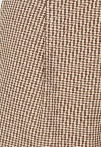 Tissu à carreaux brun et blanc avec une surface texturée, présentant de petits motifs en croix disposés en grille, adapté pour les vêtements ou la tapisserie.