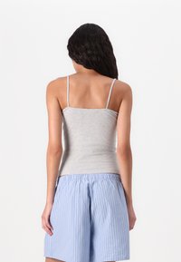 Gray cotton tank top with thin straps, fitted design, paired with blue and white striped loose shorts. Smooth texture, no visible hardware.
