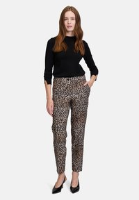 Spodnie w cętki z miękkiego materiału o dopasowanym fasonie, z kieszeniami i średnim stanem, zestawione z czarną bluzką i szpilkami.