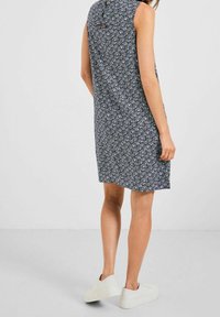 Marineblaues ärmelloses Kleid mit floralem Muster, weichem Stoff, A-Linien-Schnitt, Knopfdetail am Rücken, getragen mit weißen Sneakers.
