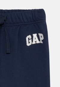 Mörkblå mjukisbyxor med elastiskt midjeband, utrustade med dragsko och broderad "GAP"-logotyp i vitt på övre vänstra sidan.