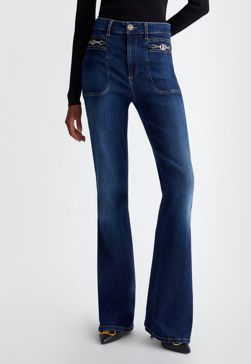 Jeans in denim blu svasati con alta vita, dotati di tasche frontali e dettagli in metallo dorato. Texture liscia e design classico.