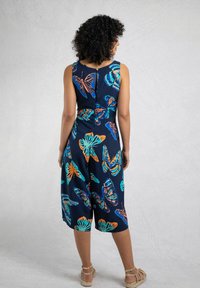 Navy blue jumpsuit with butterfly print in orange and teal, featuring a fitted bodice, wide legs, and a back button closure.