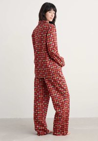 Vörös mintás pizsama szett, sárga és kék geometrikus mintákkal. Az anyag simának tűnik, laza szabású, hosszú ujjal.