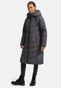 Grey puffer coat with a long cut, chevron pattern, adjustable hood, and front zipper. Paired with dark jeans and black lace-up boots.