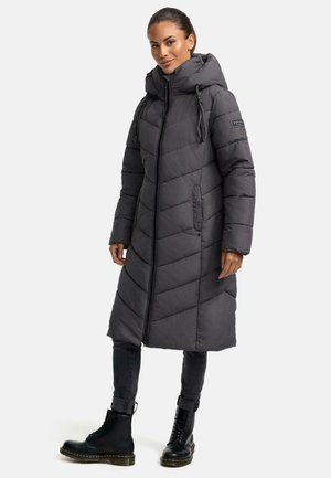 Graue Pufferjacke mit langem Schnitt, Zickzackmuster, verstellbare Kapuze und Frontreißverschluss. Kombiniert mit dunklen Jeans und schwarzen Schnürstiefeln.