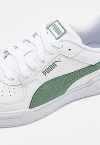Baskets blanches Puma avec bande latérale verte et logo, lacets blancs, et dessus en cuir texturé en gros plan.