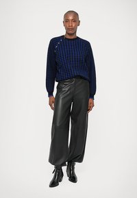 Σουέτερ σε ναυτικό μπλε χρώμα με σχέδιο καρό, στρογγυλή λαιμόκοψη και ρίγες στις μανσέτες, συνδυασμένο με φαρδιά μαύρα δερμάτινα παν trousers και μποτάκια μέχρι τον αστράγαλο.