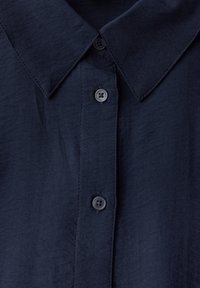 Camicia button-up di un blu scuro navy con colletto strutturato, dotata di quattro bottoni coordinati, tessuto liscio e una leggera lucentezza.
