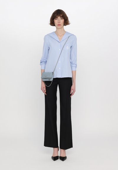 Himmelblau gestreiftes Hemd mit Kapitänskragen, kombiniert mit schwarzen Weitbein-Hosen und einer kleinen blauen Umhängetasche mit Kettenriemen.