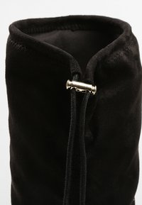 Tige de botte en daim noir avec un cordon noir serré par un petit stoppeur doré métallique en haut.