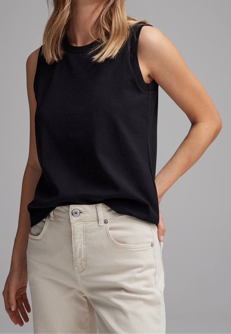 Haut sans manches noir en tissu lisse, associé à un jean beige clair avec poches avant et fermeture à bouton classique.