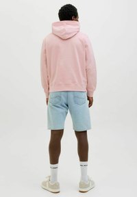 Roze hoodie, lichtblauwe denim shorts, witte sokken met logo en beige sneakers. Soepele textuur en casual ontwerp.