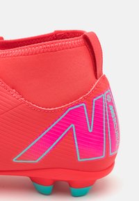 Crampons de soccer rouges avec une texture lisse, présentant un design rose et un accent bleu sur la semelle. Le talon a une structure renforcée pour le soutien.