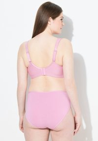 Vaaleanpunainen liivi ja korkeavyötäröiset alushousut, jotka on valmistettu sileästä kankaasta, joissa on säädettävät olkaimet, kiinnitysneula ja saumaton reuna.