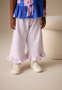 Ru žové a modré nohavice so vzorom káro a volánikovými manžetami, v kombinácii s bielymi teniskami. Hladká tkanina s voľným strihom a ľahkou textúrou.