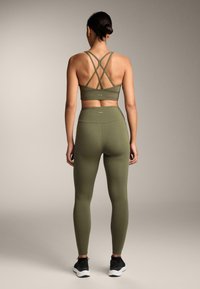 Olívazöld sportmelltartó keresztpántos kialakítással, hozzáillő, magas derekú leggingsszel párosítva. Simább, rugalmas anyagból készült.