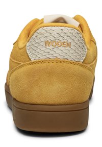 Gelbe Wildledersneaker mit einem strukturierten beigen Rückenteil, auf dem "WOODEN" gestickt ist. Gummisohle und gepolsterter Kragen sorgen für Komfort.