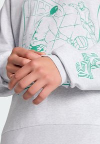 Sudadera gris claro de tela suave con estampado gráfico verde que muestra imágenes deportivas y marcas en la manga. Puños ajustados visibles.