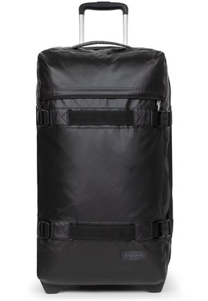 Black roller suitcase made of durable material, featuring a telescoping handle, side straps, and a logo patch at the base. Smooth texture.