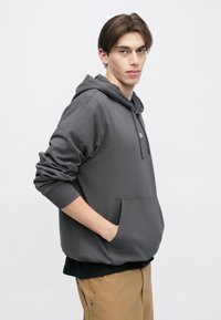 Γκρι φούτερ με κουκούλα, τσέπη κάγκουρα, ριμπ μανσέτες και τελείωμα. Το ύφασμα έχει λεία υφή και ένα διακριτικό λογότυπο στο στήθος.