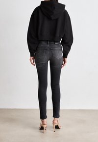 Sudadera negra recortada, jeans ajustados grises con bolsillos traseros y tacones beige con tiras. Tejido suave con un ajuste ceñido y detalles mínimos.