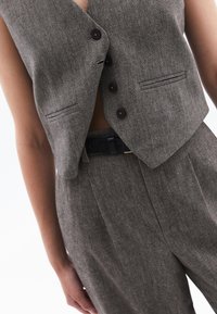 Grå herringbone-väst med en figurnära design, med djup V-ringning, tre mörka knappar och sidofickor, sammansatt med matchande byxor.