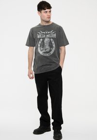 Gray graphic t-shirt featuring "Willie Nelson" text and an outlaw motif, paired with black pants and black boots. Front view.