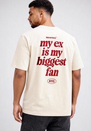 Ein Mann, der von hinten zu sehen ist, trägt ein beigefarbenes T-Shirt mit großem roten Text auf dem Rücken, der "my ex is my biggest fan" lautet, und kleineren "Neverless" und "NVL" Logos.
