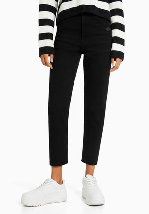 Black skinny jeans with a high waist and distressed detailing, paired with a black and white striped sweater and white sneakers.