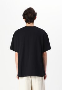 T-shirt en coton noir à manches courtes et à coupe décontractée, avec un col rond classique, une texture unie et sans logos ni motifs visibles.