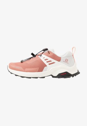 Chaussure de sport rose clair avec empeigne en maille, accents blancs, semelle noire et système de laçage à bascule. Dispose d'un logo sur le talon et des bandes latérales.