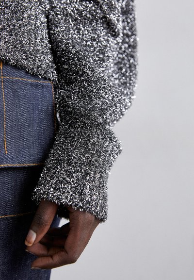 Lun gra sweater med metalltråde, der har løse ærmer. Kombineret med mørk denim, der fremhæver synlige stingdetaljer.