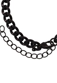 Collana in catena nera con un design spesso e intrecciato, caratterizzata da una superficie liscia e una chiusura a fermaglio, accompagnata da una catena più piccola.