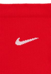 Calza di cotone rossa con un bordo a coste e il logo Nike swoosh bianco. La texture liscia e il design semplice mettono in risalto il colore audace.