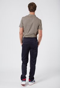 Koszulka polo z krótkim rękawem w geometryczny wzór w odcieniach beżu, granatu i zieleni, sparowana z granatowymi spodniami i białymi sneakersami z czerwonymi akcentami.