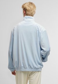 Helleblau, weiche Stoffjacke mit hohem Kragen, elastischem Saum und langen Ärmeln. Die Rückansicht zeigt eine glatte Textur und eine lockere Passform.