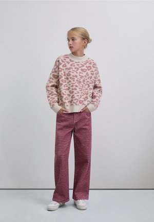 Suéter de punto en color crema con estampado de leopardo rosa, combinado con vaqueros holgados de color rosa oscuro con estampado de rayas de cebra y zapatillas blancas.