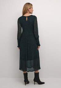 Vihreä pitkähihaisen mekko, jossa on smocked-paita ja avopartaat takaosa; kerroksellinen, läpikuultava kangas; yhdistetty mustiin nilkkabootseihin.