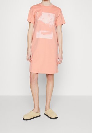 Jasnoróżowa sukienka t-shirtowa wykonana z bawełny, z przodem ozdobionym grafiką palm i basenu, z krótkimi rękawami i prostym krojem.