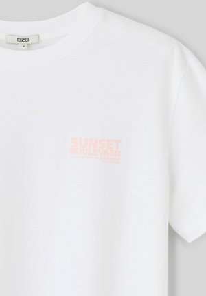 T-shirt blanc à manches courtes avec un petit texte rose fané « Sunset Boulevard, Los Angeles, California » sur la poitrine gauche.
