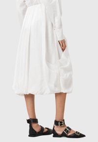 Czarne skórzane sandały z paskami na kostkach, złotym zapięciem oraz spiczastymi noskami, zestawione z białą, teksturowaną spódnicą do kolan.