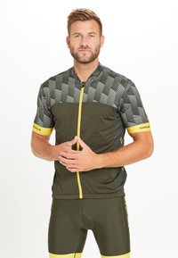 Maillot de cyclisme vert avec un motif à carreaux en haut, fermeture éclair jaune et accents, associé à un short vert assorti avec des bordures jaunes.