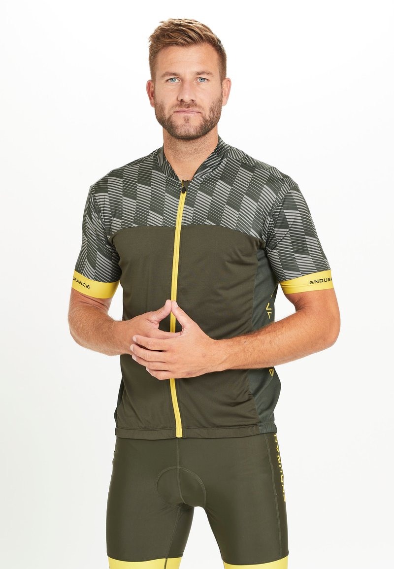 Maillot de cyclisme vert avec un motif à carreaux en haut, fermeture éclair jaune et accents, associé à un short vert assorti avec des bordures jaunes.
