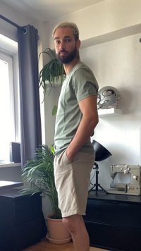 Šviesiai žalias medvilnės marškinėlis ir smėlio spalvos šortai, stovintys viduje šalia augalo ir juodos unitos, kur matomi siuvimo mašina ir šalmą.