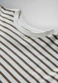 Primer plano de una camiseta blanca con cuello redondo y rayas horizontales marrones sobre una superficie plana.