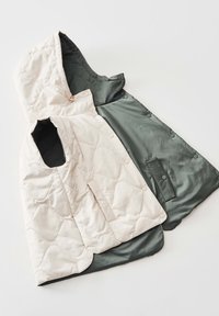 Gepolsterte Weste in Hellbeige und Dunkelgrün, mit Kapuze, Druckknöpfen und einer Tasche, die eine glatte Textur und ein geschichtetes Design zeigt.