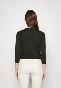 Schwarzer leichter Strickpullover mit drei Viertelärmeln, Rundhalsausschnitt und geripptem Saum. Getragen mit weißen, engen Hosen.