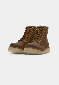 Bottines en cuir marron avec des orteils arrondis, un laçage à l'avant et des œillets en métal. Semelles en caoutchouc beige épaisses offrant une bonne adhérence.